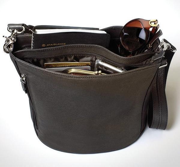 Elegant concealed carry bucket tote made of full grain tumbled leather with dual vertical zip access for left or right-hand draw, slash-resistant crossbody strap, and double main compartments with organized storage.