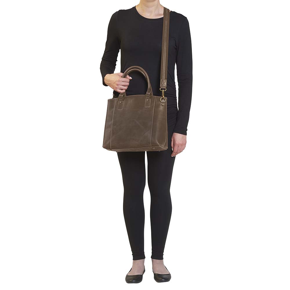 Distressed brown full grain buffalo leather town tote with concealed carry compartment. Vintage-inspired patina develops with use. Features reinforced slash-resistant shoulder strap, padded interior for gun protection, and dual top handles for versatile carry. Designed for ambidextrous draw, includes multiple pockets for phone, pepper spray, and essentials. Tested with popular pistols, equipped with Mernickle holster. Durable and stylish everyday concealed carry purse.