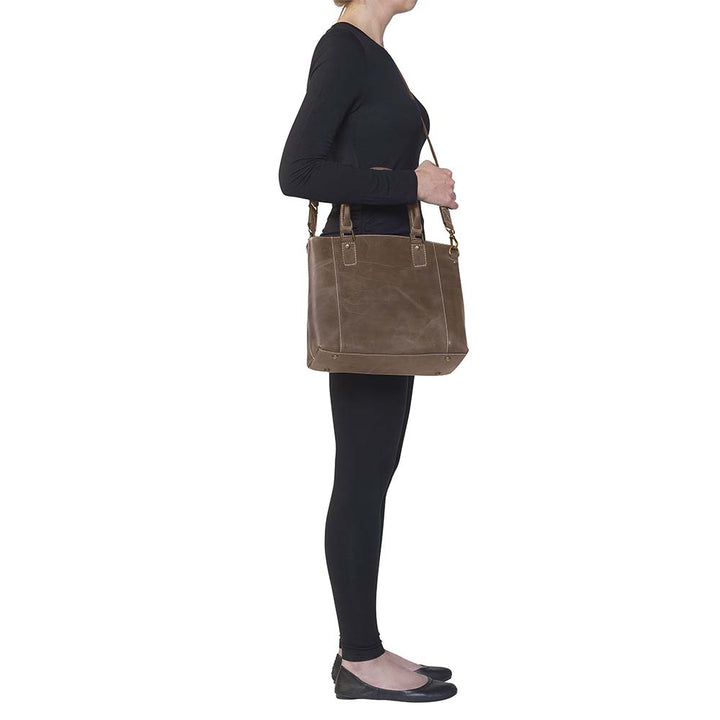 Distressed brown full grain buffalo leather town tote with concealed carry compartment. Vintage-inspired patina develops with use. Features reinforced slash-resistant shoulder strap, padded interior for gun protection, and dual top handles for versatile carry. Designed for ambidextrous draw, includes multiple pockets for phone, pepper spray, and essentials. Tested with popular pistols, equipped with Mernickle holster. Durable and stylish everyday concealed carry purse.
