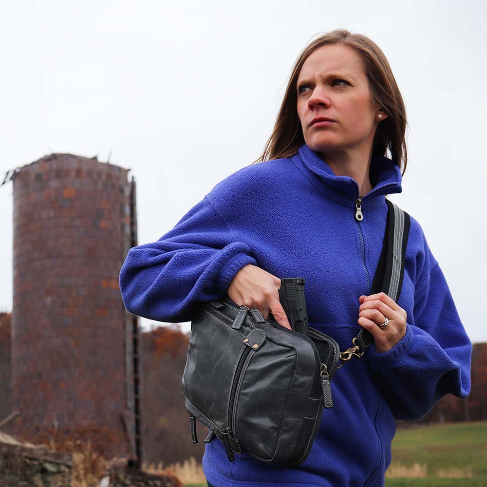 Roman carrying a Gray sling backpack concealed carry bag pulling out a ccw with RFID protection, ambidextrous draw, and padded CCW compartment; lightweight crossbody made for quick access, featuring slash-resistant strap, fits Glock 19, Sig P365, M&P 9mm, and ideal for everyday or EDC use.