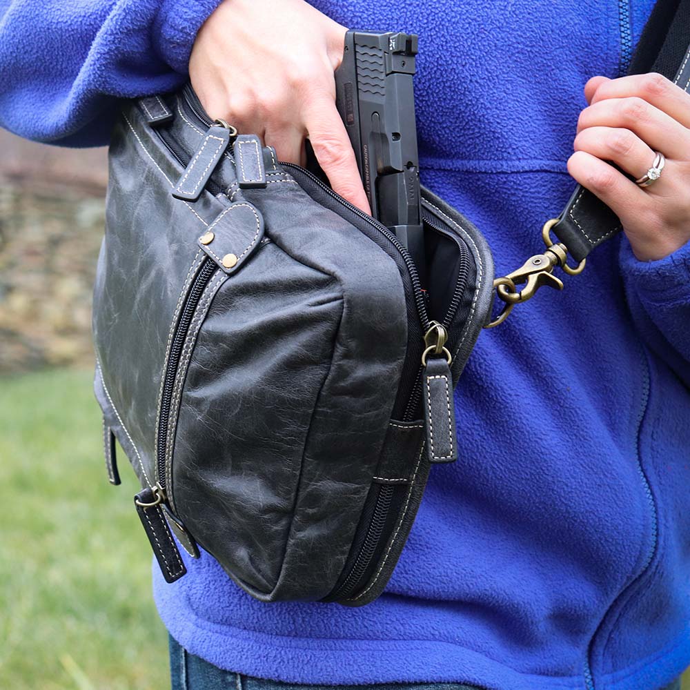close up of a woman pulling out a gray sling backpack concealed carry bag with RFID protection, ambidextrous draw, and padded CCW compartment; lightweight crossbody made for quick access, featuring slash-resistant strap, fits Glock 19, Sig P365, M&P 9mm, and ideal for everyday or EDC use.