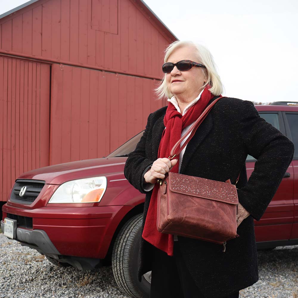 woman carrying a distressed full-grain buffalo leather clutch gets better with age and wear. Designed to fit both left and right-handed carriers, it offers special padding to prevent imprinting and a slash-resistant shoulder strap reinforced with 11-ply steel wire for solid security.