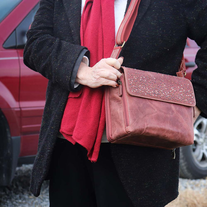 close up of a woman carrying a distressed full-grain buffalo leather clutch gets better with age and wear. Designed to fit both left and right-handed carriers, it offers special padding to prevent imprinting and a slash-resistant shoulder strap reinforced with 11-ply steel wire for solid security.