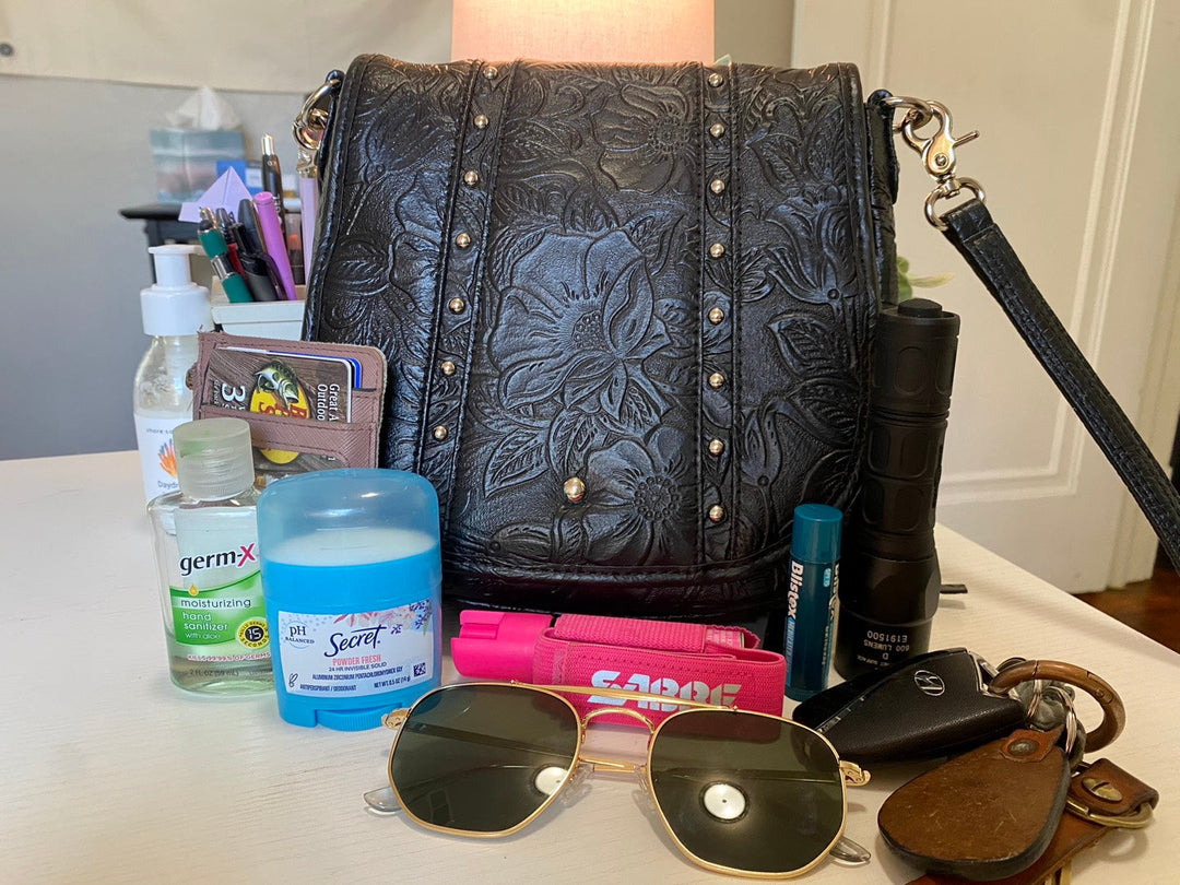 Open GTM purse on a table surrounded by personal items like sunglasses, lotion, lip balm, and keys.