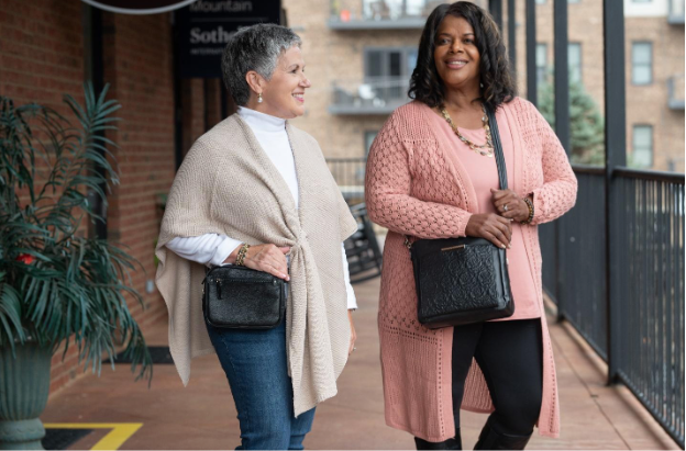 Two women smiling on a city street, each wearing a concealed carry purse with cozy fall outfits.