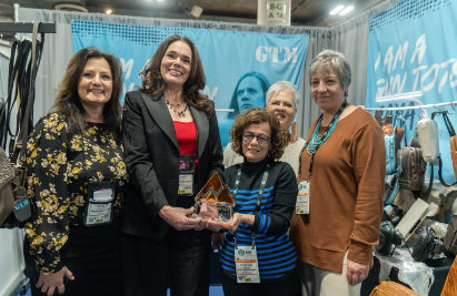  Receiving the Safe LivinG Annual Excellence in Safety Award Group of women smiling and posing together at a tradeshow booth, one holding an award trophy.