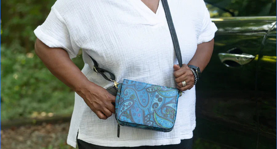 Five New Colorful Concealed Carry Purses for Spring: Fashion Meets Function Close-up of a person wearing a white blouse and holding a vibrant blue paisley-patterned crossbody concealed carry purse.