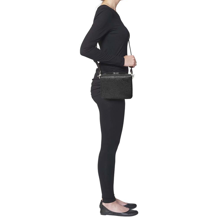 girl from side holding a lightweight black crossbody organizer made from debossed American cowhide with rose leaf tooling, secure RFID zippered compartment, slash-resistant strap, adjustable and removable shoulder strap, includes mini holster compatible with Crossbreed holsters.