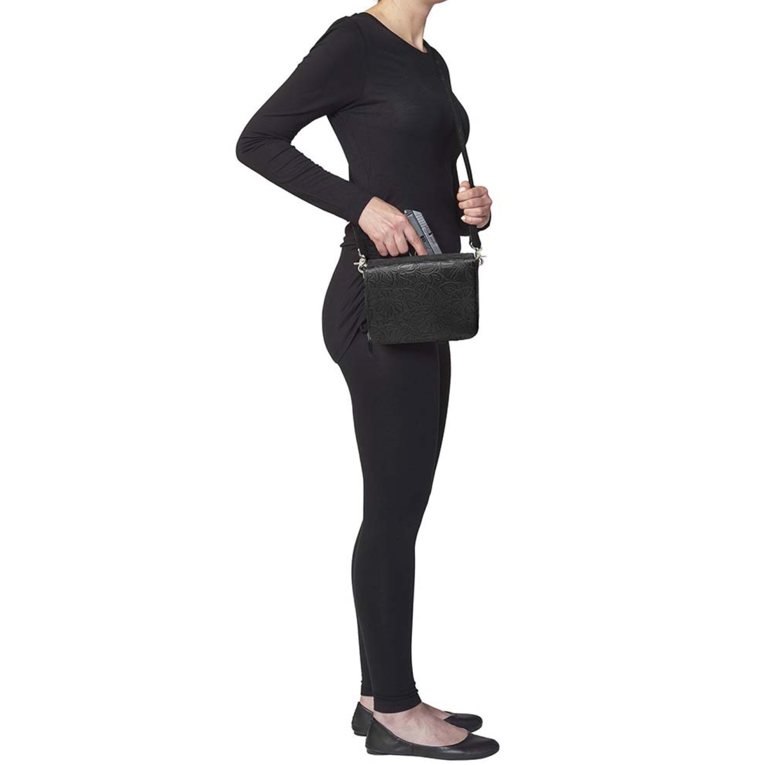girl pulling gun out of a Lightweight black crossbody organizer made from debossed American cowhide with rose leaf tooling, secure RFID zippered compartment, slash-resistant strap, adjustable and removable shoulder strap, includes mini holster compatible with Crossbreed holsters.