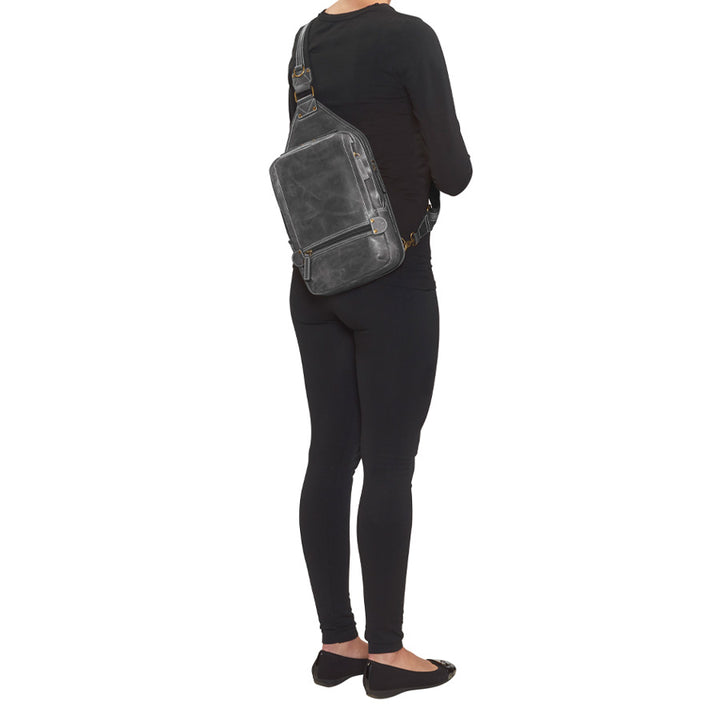 model from the back with Distressed gray buffalo leather sling concealed carry backpack with tactical organization, RFID zip pocket, padded holster compartment for Glock 19, Sig P320, and HK VP9, slash-proof strap, and swing-front crossbody design with 3 exterior zip pockets and morale patch zone