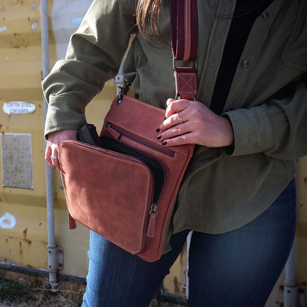 close up of model gripping pistol in the Vintage distressed buffalo leather concealed carry crossbody purse with adjustable slash-resistant strap, left and right-handed access, and a secure gun compartment designed for fast draw. Includes holster and fits compact handguns like S&W Shield, Ruger LCP, and Glock 42.