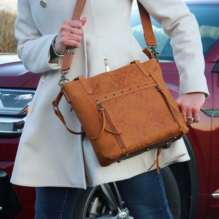 girl in a city with a tan concealed carry BOHO tote purse with top-access CCW compartment, symbolic butterfly and flower debossed leather, slash-proof straps, RFID-blocking zip pocket, and room for compact pistols like CZ P10, M&P Shield, and S&W EZ—each bag uniquely aged from natural tanning.