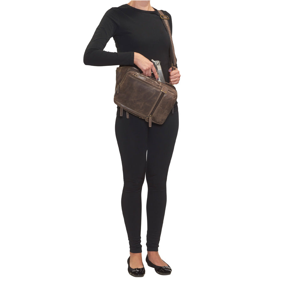 model with front draw of a gun with a Distressed brown buffalo leather sling concealed carry backpack with tactical organization, RFID zip pocket, padded holster compartment for Glock 19, Sig P320, and HK VP9, slash-proof strap, and swing-front crossbody design with 3 exterior zip pockets and morale patch zone