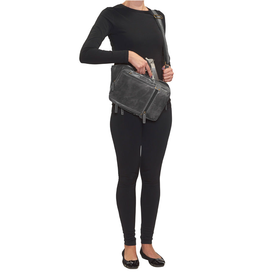 model holding gun from Distressed gray buffalo leather sling concealed carry backpack with tactical organization, RFID zip pocket, padded holster compartment for Glock 19, Sig P320, and HK VP9, slash-proof strap, and swing-front crossbody design with 3 exterior zip pockets and morale patch zone