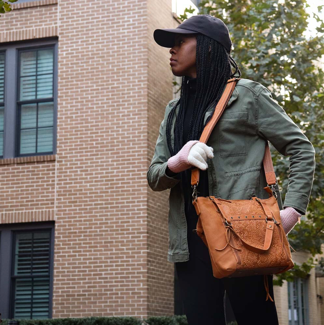 woman in a big city with a tan concealed carry BOHO tote purse with top-access CCW compartment, symbolic butterfly and flower debossed leather, slash-proof straps, RFID-blocking zip pocket, and room for compact pistols like CZ P10, M&P Shield, and S&W EZ—each bag uniquely aged from natural tanning.