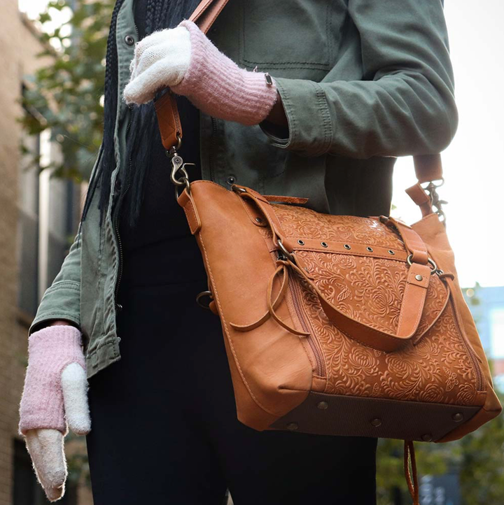 Woman in city with a Tan concealed carry BOHO tote purse with top-access CCW compartment, symbolic butterfly and flower debossed leather, slash-proof straps, RFID-blocking zip pocket, and room for compact pistols like CZ P10, M&P Shield, and S&W EZ—each bag uniquely aged from natural tanning.